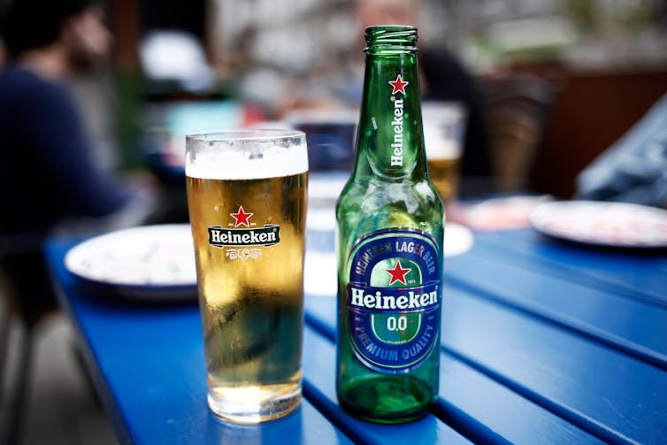 Une bouteille de bière Heineken 0 % et un verre de bière avec l’étiquette Heineken sur une table bleue